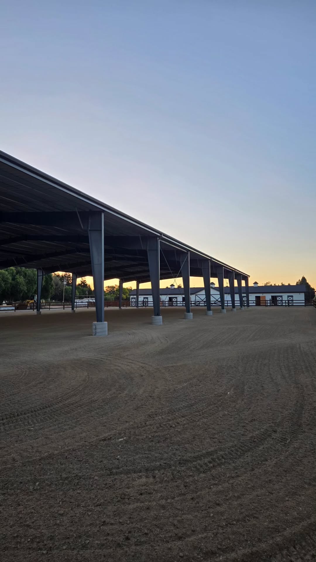 Steel-covered arena at dusk, with the Cavalli stable building beyond