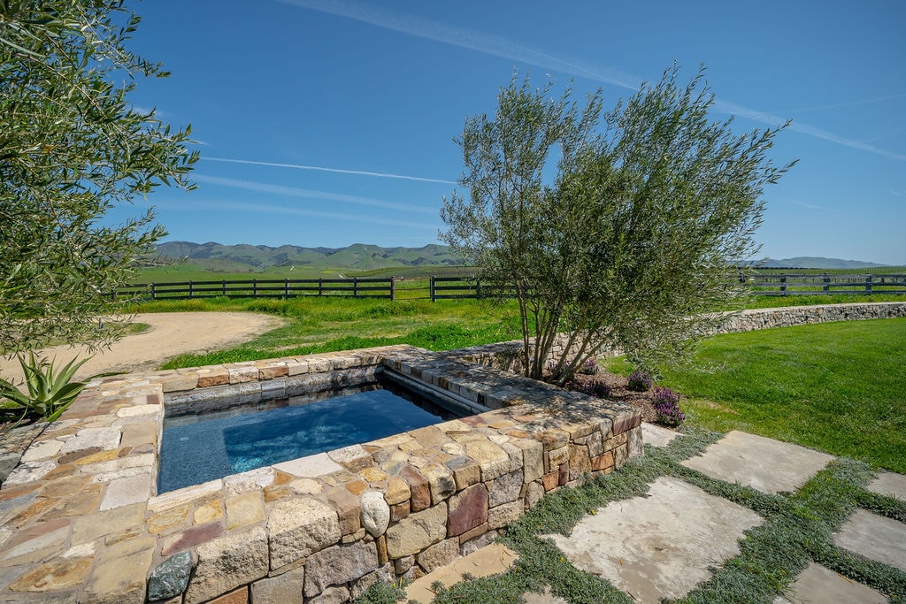 Stone-lined outdoor spa with lawn and hills beyond
